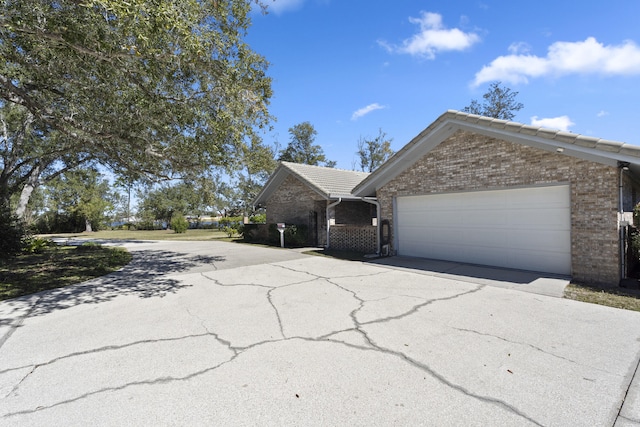 view of property exterior featuring a garage, brick siding, driveway, and a tile roof