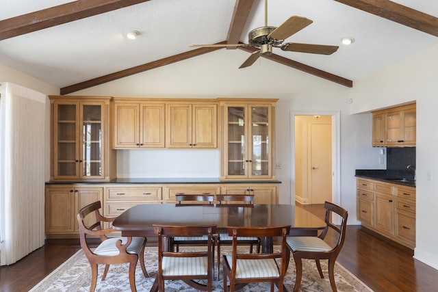 dining area featuring a ceiling fan, vaulted ceiling with beams, dark wood-style floors, and baseboards