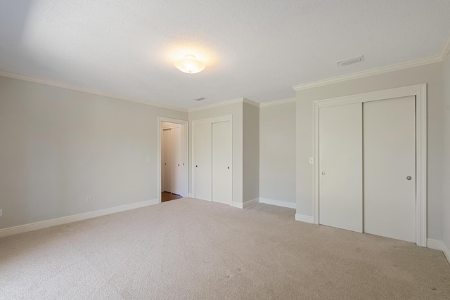 unfurnished bedroom featuring visible vents, multiple closets, carpet floors, and ornamental molding