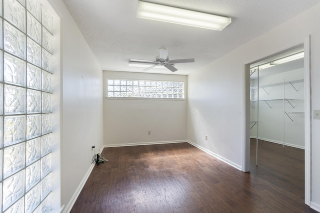 unfurnished bedroom featuring a walk in closet, baseboards, wood finished floors, a textured ceiling, and a ceiling fan