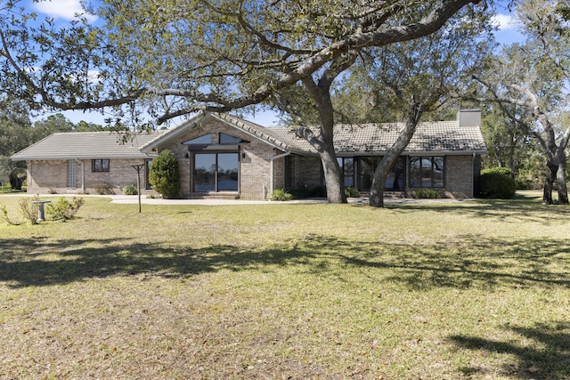 view of front of house featuring brick siding, a chimney, a tile roof, and a front lawn