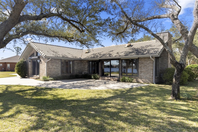 single story home featuring entry steps, a front lawn, a tiled roof, and brick siding