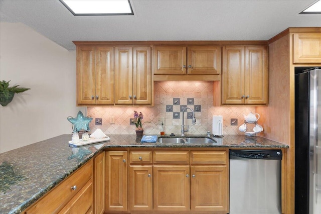 kitchen featuring dark stone counters, stainless steel appliances, a sink, and decorative backsplash