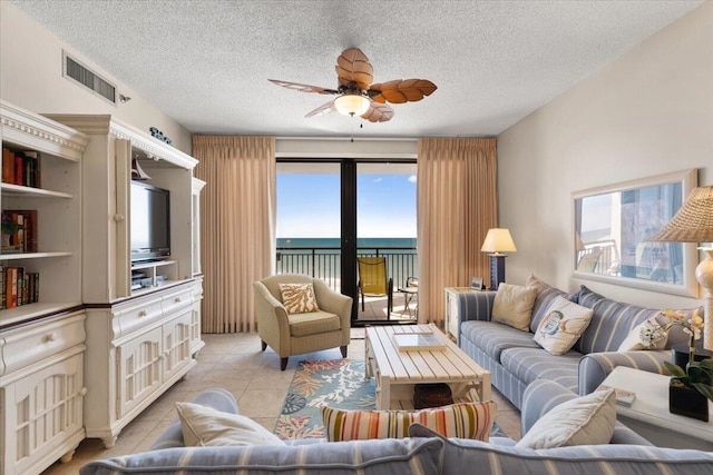 living room with light tile patterned floors, ceiling fan, visible vents, and a textured ceiling