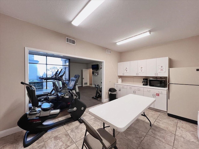 kitchen featuring black microwave, visible vents, white cabinetry, light countertops, and freestanding refrigerator