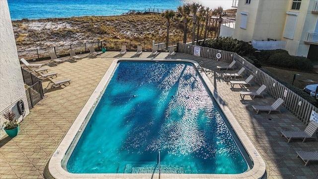 community pool with a water view, a patio area, and fence