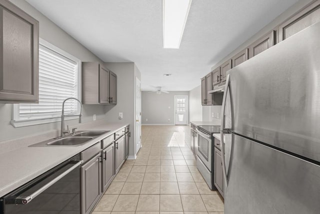 kitchen featuring light tile patterned floors, gray cabinets, appliances with stainless steel finishes, a sink, and under cabinet range hood