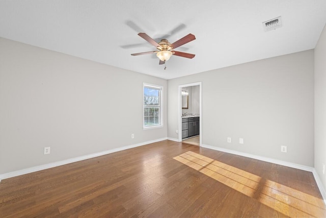 unfurnished room with baseboards, visible vents, dark wood finished floors, and a ceiling fan