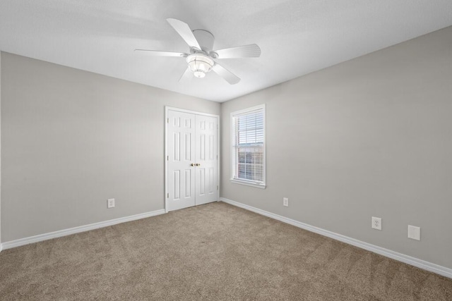 carpeted spare room featuring ceiling fan and baseboards