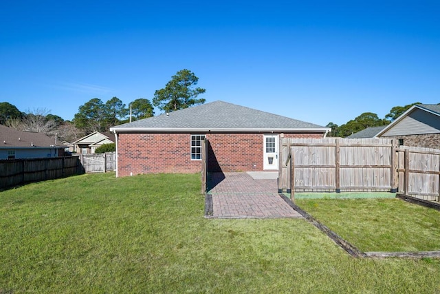 back of house featuring a fenced backyard, brick siding, a yard, roof with shingles, and a patio area