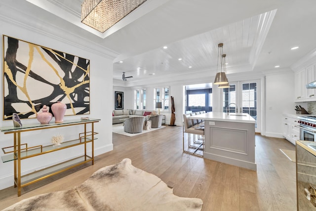 kitchen featuring a tray ceiling, ornamental molding, light wood-style floors, white cabinets, and a sink