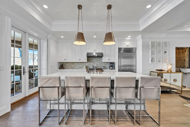 kitchen with stainless steel built in fridge, under cabinet range hood, a tray ceiling, and light countertops