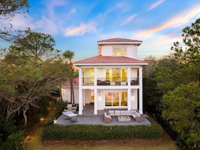 back of house at dusk featuring a balcony, a tiled roof, and stucco siding