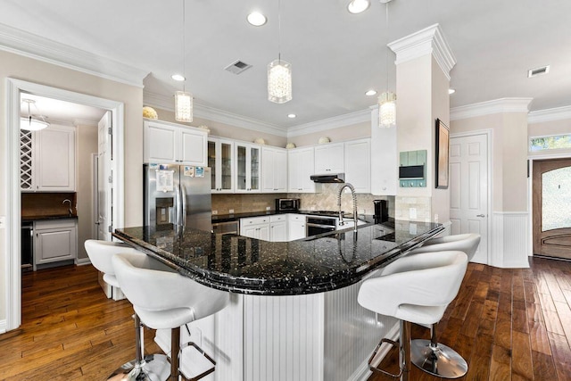 kitchen featuring under cabinet range hood, a sink, visible vents, white cabinets, and stainless steel fridge