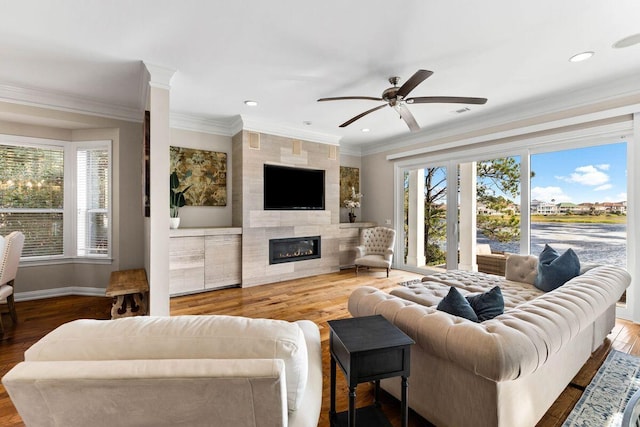 living room featuring baseboards, a tiled fireplace, ceiling fan, wood finished floors, and crown molding