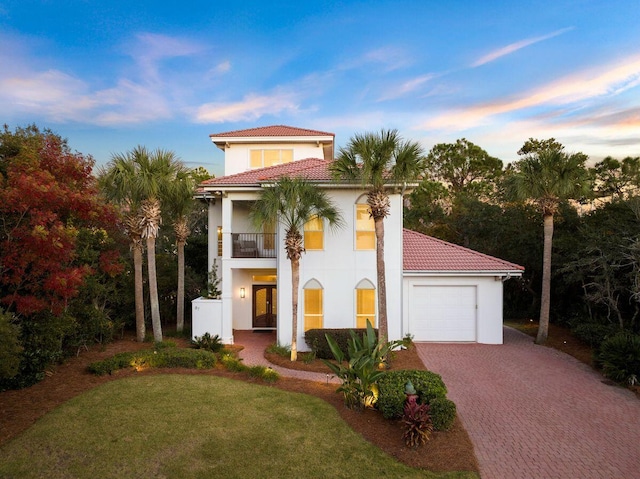 mediterranean / spanish-style house featuring decorative driveway, stucco siding, a balcony, a garage, and a tiled roof