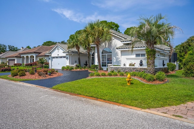 mediterranean / spanish home featuring driveway, a front lawn, an attached garage, and a tile roof