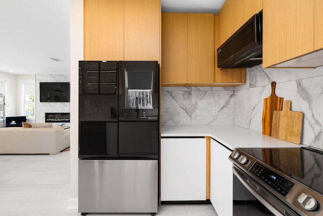 kitchen featuring stainless steel electric range oven, light countertops, a high end fireplace, freestanding refrigerator, and black microwave