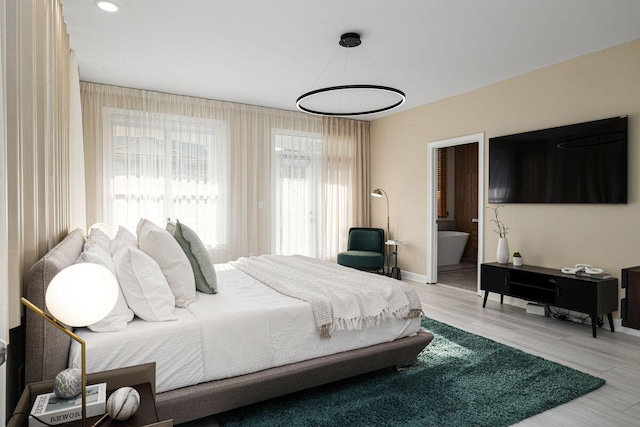 bedroom with ensuite bath, light wood-style flooring, and baseboards