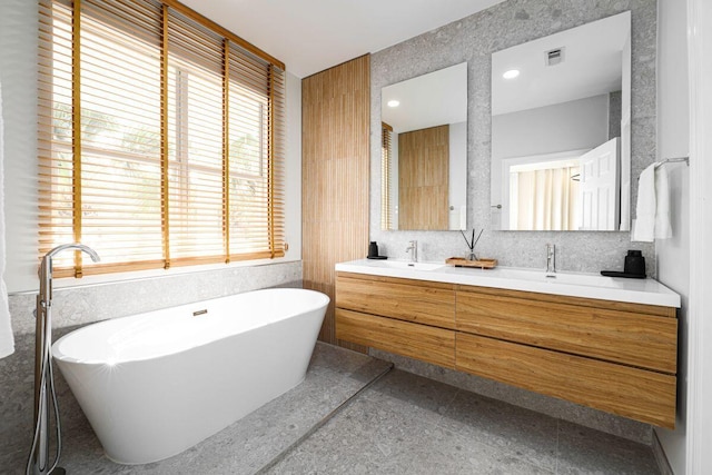 full bath with double vanity, visible vents, a soaking tub, granite finish floor, and a sink