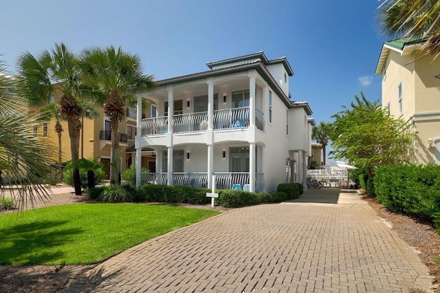 view of front of home with decorative driveway, a front yard, a balcony, and stucco siding