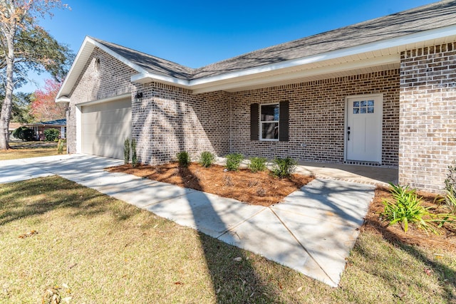 entrance to property with a garage, a yard, concrete driveway, and brick siding