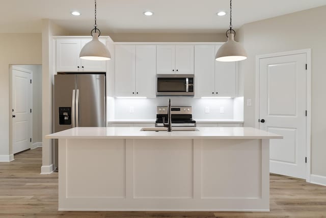 kitchen with light wood-style flooring, stainless steel appliances, a sink, white cabinets, and tasteful backsplash