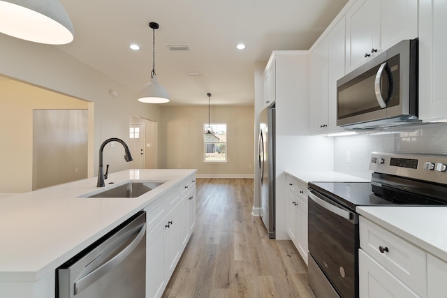 kitchen with stainless steel appliances, a sink, light countertops, decorative backsplash, and light wood finished floors