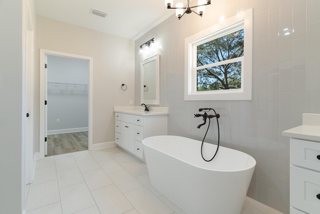 full bathroom featuring vanity, visible vents, tile walls, a spacious closet, and a soaking tub