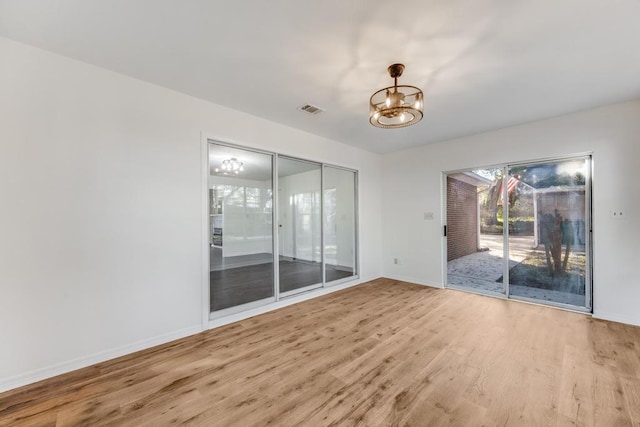 empty room with visible vents, baseboards, an inviting chandelier, and wood finished floors