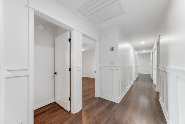 corridor featuring dark wood-style floors, a decorative wall, wainscoting, and attic access