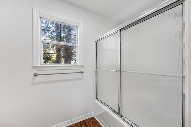 bathroom featuring combined bath / shower with glass door, baseboards, and wood finished floors