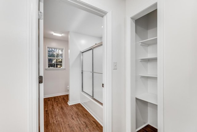 bathroom featuring baseboards, shower / bath combination with glass door, wood finished floors, and toilet