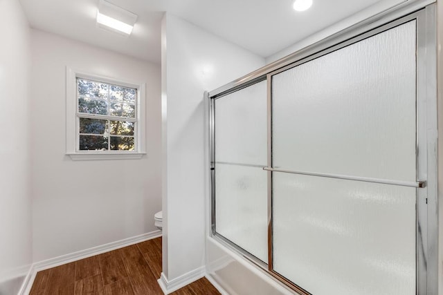 bathroom with toilet, combined bath / shower with glass door, wood finished floors, and baseboards