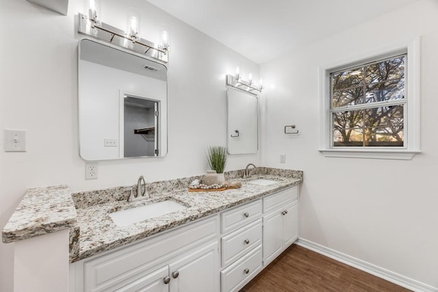 full bath with double vanity, wood finished floors, baseboards, and a sink