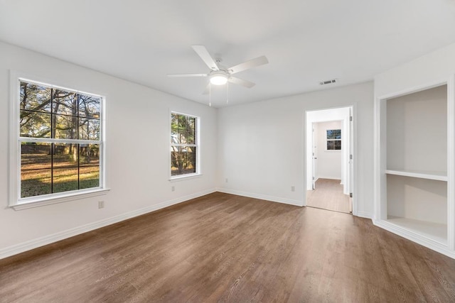 spare room with visible vents, built in shelves, a ceiling fan, wood finished floors, and baseboards