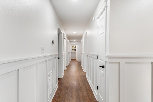 hallway with a wainscoted wall, a decorative wall, dark wood-style floors, and visible vents