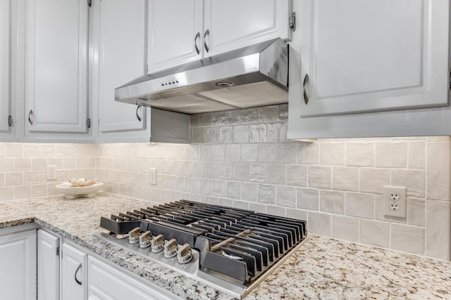 kitchen with backsplash, light stone countertops, under cabinet range hood, stainless steel gas cooktop, and white cabinetry