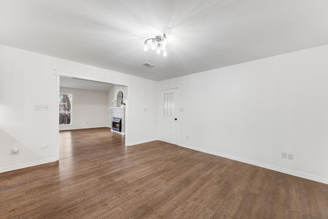 unfurnished living room with visible vents, baseboards, dark wood-type flooring, and a warm lit fireplace