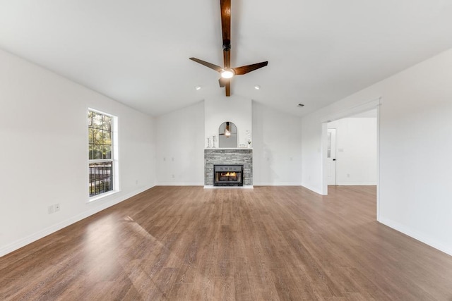 unfurnished living room with a stone fireplace, lofted ceiling with beams, wood finished floors, and baseboards