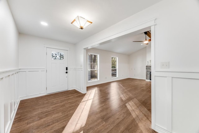 entryway with wood finished floors, a wainscoted wall, lofted ceiling, ceiling fan, and a stone fireplace