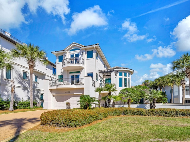 mediterranean / spanish-style house featuring a garage, a balcony, stucco siding, decorative driveway, and a front yard