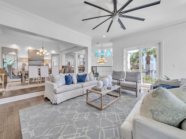 living area with ceiling fan with notable chandelier, ornamental molding, and wood finished floors