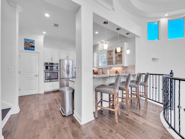 kitchen featuring light wood finished floors, decorative backsplash, light stone countertops, white cabinetry, and a sink