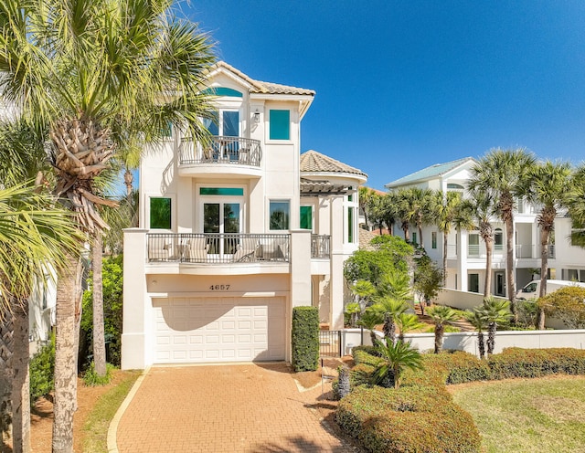 view of front of house featuring decorative driveway, a balcony, an attached garage, and stucco siding