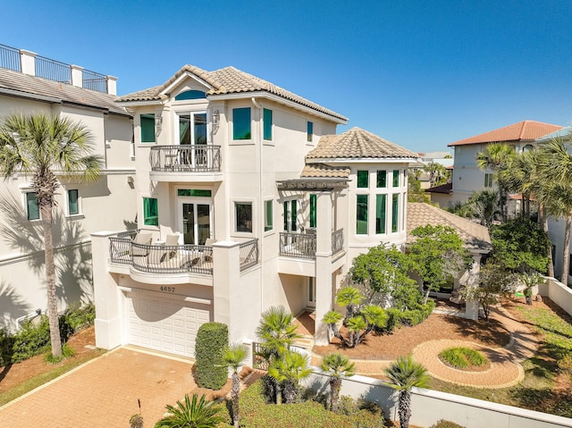 rear view of property featuring a balcony, a tile roof, decorative driveway, and stucco siding