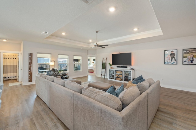 living room with visible vents, a tray ceiling, light wood-style flooring, and baseboards