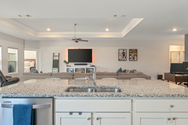 kitchen with a tray ceiling, open floor plan, a sink, and stainless steel dishwasher