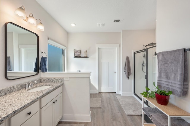 full bath with wood finished floors, vanity, visible vents, baseboards, and a stall shower