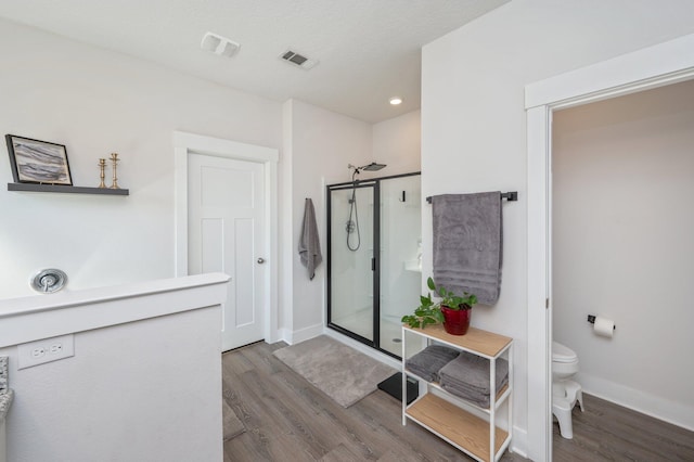 bathroom featuring toilet, a stall shower, wood finished floors, and visible vents